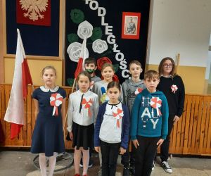 Uczniowie stoją na tle gazetki upamiętniającej Święto Niepodległości