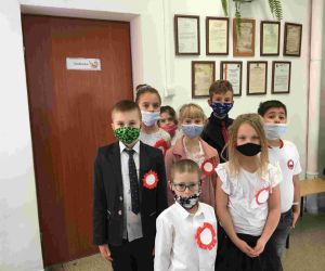 Uczniowie klasy II w strojach galowych i maskach, z przypiętymi kotylionami w barwach narodowych.