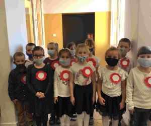 Przedszkolaki w strojach galowych i maskach, z przypiętymi kotylionami w barwach narodowych.