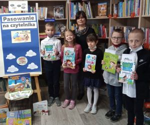 Zdjęcie przedstawia bibliotekarkę i grupę dzieci w bibliotece.