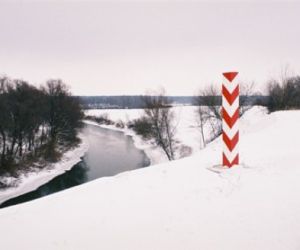 Zimowa panorama, skarpa w dole rzeka, krzewy i drzewa, na pierwszym planie czerwono-biały słupek graniczny