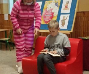 Pani nauczycielka przebrana za misia stoi przy uczniu, który czyta książkę o Kubusiu Puchatku