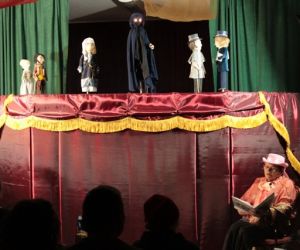 Kukiełki w przedstawieniu teatrzyku kukiełkowym. Narrator siedzi przed parawanem.