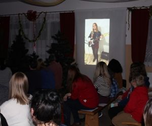 Zdjęcie przedstawia wyświetloną na ekranie dziewczynkę grającą na gitarze.