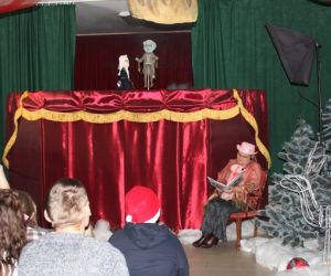 Kukiełki w przedstawieniu teatrzyku kukiełkowym. Narrator siedzi przed parawanem.