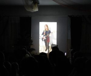 Zdjęcie przedstawia wyświetloną na ekranie dziewczynkę grającą na gitarze.