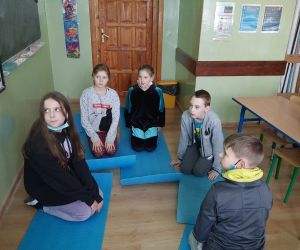 Uczniowie siedzą na matach i naśladują postaci z baśni