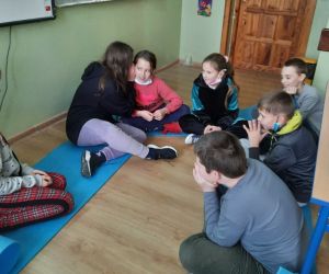 Uczniowie siedzą w kręgu i bawią się w głuchy telefon