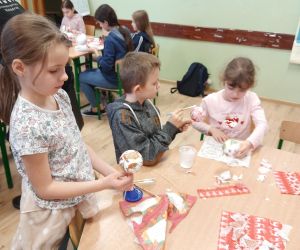 Uczniowie klasy pierwszej przyklejają na bombkę elementy z papierowej serwetki