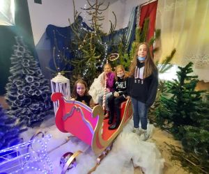 Uczniowie siedzą w saniach Mikołaja, dziewczynka stoi obok nich