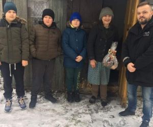 Trzech uczniów klasy piątej, starsza kobieta trzymająca stroik świąteczny i mężczyzna stoją przed wejściem do domu kobiety