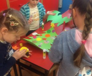 Dzieci wyklejają choinkę. 