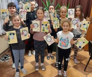 Dzieci stoją w grupie prezentują laurki wykonane podczas warsztatów.