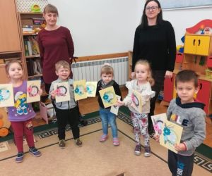 Dzieci stoją w grupie z 2 osobami dorosłymi i prezentują laurki wykonane podczas warsztatów.
