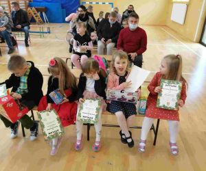 Przedszkolaki siedzą na ławce i oglądają swoje nagrody