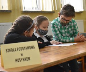 Dzieci siedzą wewnątrz budynku i rozwiązują zadania konkursowe.