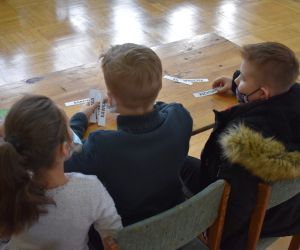Dzieci siedzą wewnątrz budynku i rozwiązują zadania konkursowe.
