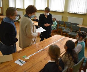 Dzieci wewnątrz budynku siedzą a Pani należące do Komisji Konkursowej przypatrują się rozwiązaniom zadania.