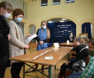 Dzieci wewnątrz budynku siedzą a Pani należące do Komisji Konkursowej przypatrują się rozwiązaniom zadania.