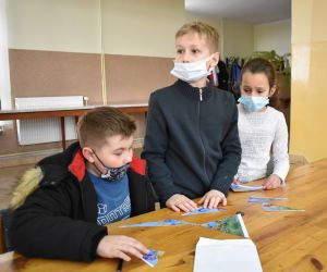 Dzieci siedzą wewnątrz budynku i rozwiązują zadania konkursowe.