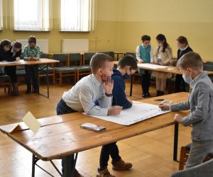 Dzieci siedzą wewnątrz budynku i rozwiązują zadania konkursowe.