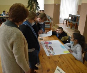 Dzieci wewnątrz budynku siedzą a Pani należące do Komisji Konkursowej przypatrują się rozwiązaniom zadania.