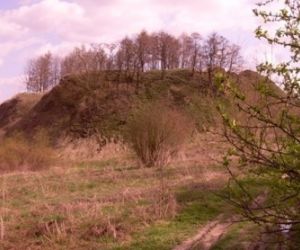Kopiec usypany z ziemi, porośnięty trawą, na górze rosną drzewa, sceneria jesienna