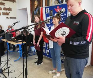 Uczniowie klasy ósmej przy mikrofonach. W tle tablica poświęcona Żołnierzom Wyklętym