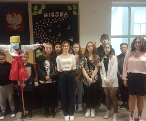 Uczniowie stoją na korytarzu z Marzanną a obok stoi dziewczynka i trzyma klucz do współrządzenia szkołą