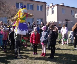 Grupa uczniów z nauczycielami przed budynkiem szkoły. Jeden z uczniów trzyma w rękach Marzannę