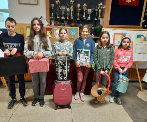 Uczniowie stoją na korytarzu,  zamiast plecaków mają wiklinowy koszyk, walizkę, segregator, pudełko prezentowe.