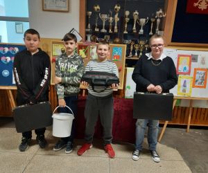 Uczniowie stoją na korytarzu,  zamiast plecaków mają walizki, wiadro i torbę turystyczną.