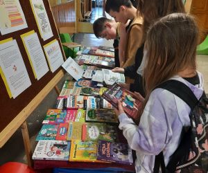 Wystawa książek na korytarzu szkolnym, nauczycielka i uczniowie przeglądają nowości wydawnicze