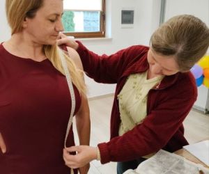 Dwie osoby wewnątrz budynku, zdejmowanie miar krawieckich.