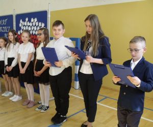 Uczniowie klasy czwartej stoją w szeregu na tle tablicy dekoracyjnej