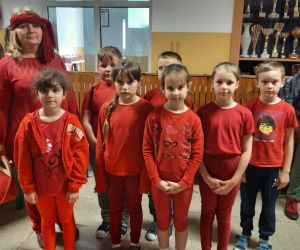 Dzieci i nauczycielka ubrani w czerwone stroje prezentują się na korytarzu szkolnym