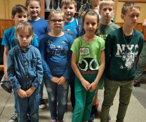 Dzieci i nauczycielka ubrani na zielono i niebiesko stoją na szkolnym korytarzu