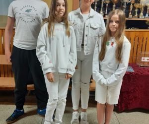 Trzy dziewczynki i chłopiec ubrani na biało stoją na szkolnym korytarzu