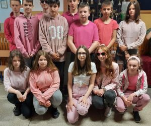 Uczniowie klasy siódmej prezentują różowe stroje na szkolnym korytarzu