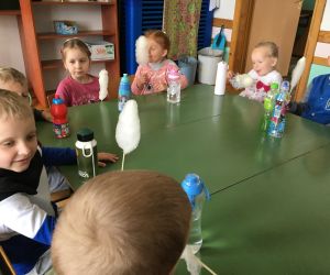 Dzieci siedzą przy stolikach i jedzą watę cukrową.