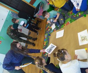 Dzieci z nauczycielem przyklejają obrazki związane z wojskiem