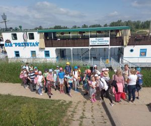 Grupa uczniów i nauczyciele stoją przy wejściu na statek wycieczkowy, w tle widać rzekę Wisłę.