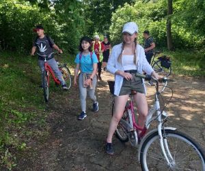 Grupa osób stoi przy rowerach na tle przyrody.