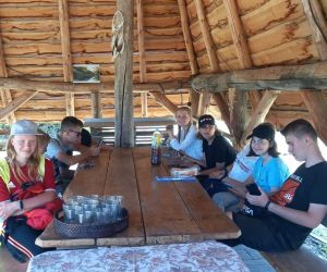 Młodzież siedzi w drewnianej wiacie przy stole.