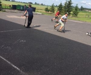 Uczniowie jeżdżą na hulajnogach na placu przed szkołą