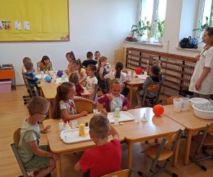 Dzieci wykonują doświadczenie z lawą, w tle stoi pani prowadząca warsztaty.