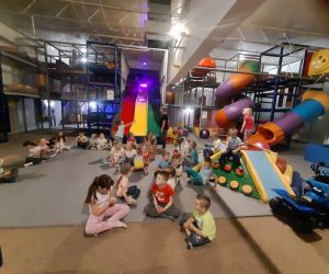 Dzieci siedzą na macie w sali zabaw.