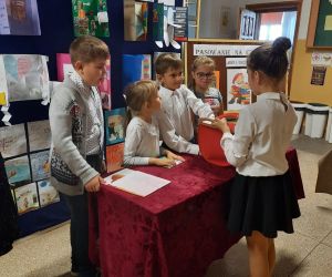 Uczennica trzyma czerwony koszyczek, z którego uczniowie losują przedmioty związane ze znanymi bajkami