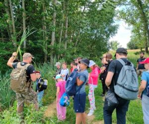 Grupa dzieci wraz z instruktorami podczas zajęć z survivalu, na świeżym powietrzu.