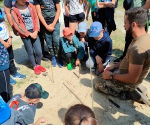 Grupa dzieci wraz z instruktorami podczas zajęć z survivalu, na świeżym powietrzu.